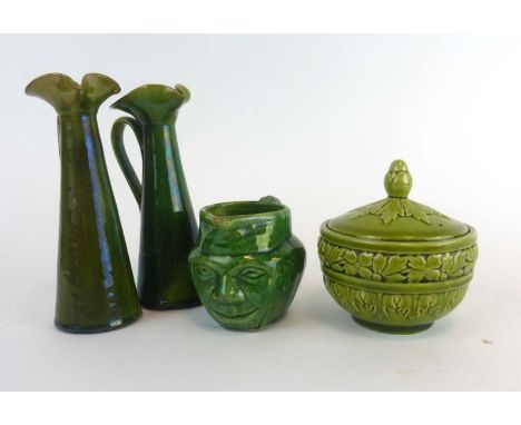 A pair of Art Nouveau slender jugs, h. 16 cm, a character jug and a Burmantofts lidded jar, all decorated in a plain green gl