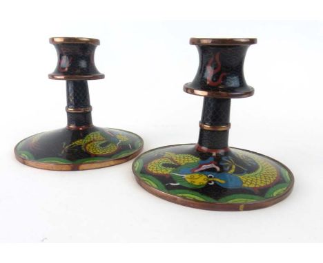 A pair of cloisonne candlesticks of traditional form decorated with a pair of dragons on a famille noir ground, h. 10 cm COND