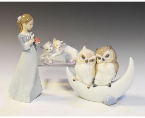 Three Nao porcelain figures to include; two owls sat on a crescent moon, woman holding a heart and two cats resting on a cush