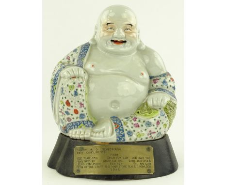 A Chinese porcelain seated Buddha, painted enamel robes, on wooden stand with presentation plaque dated 1946, overall height 