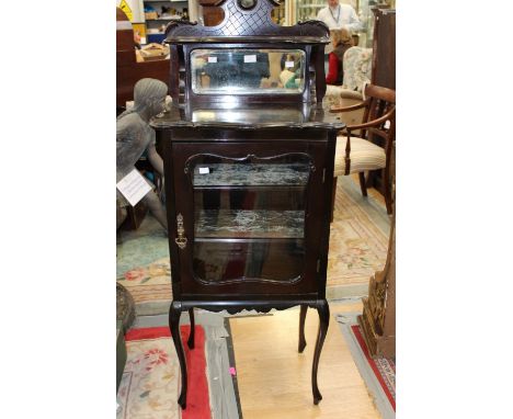 An Edwardian ebonised music cabinet, the back with an inset mirror, the front with a single glazed door enclosing two removab