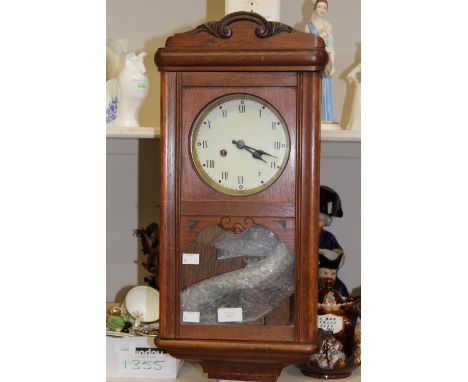 An early 20th Century oak cased wall clock, the glazed door enclosing a white enamelled dial with two winder holes 