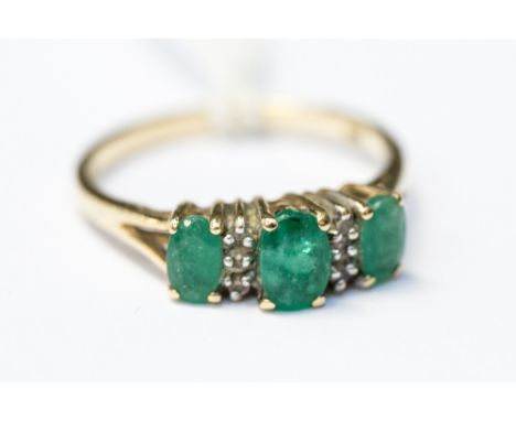 A three stone emerald and diamond ring, claw set in 9ct gold inter spaced with small diamonds, size M with a total gross weig