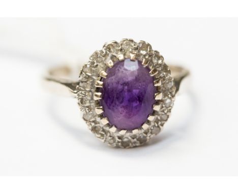 An amethyst and diamond cluster ring set in 18ct gold, comprising an oval amethyst with a scalloped surround set with diamond