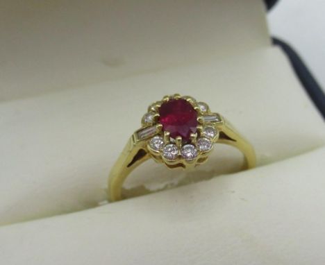 Hallmarked 18ct yellow gold diamond and ruby cluster ring with central oval cut ruby, ten round cut diamonds and two emerald 