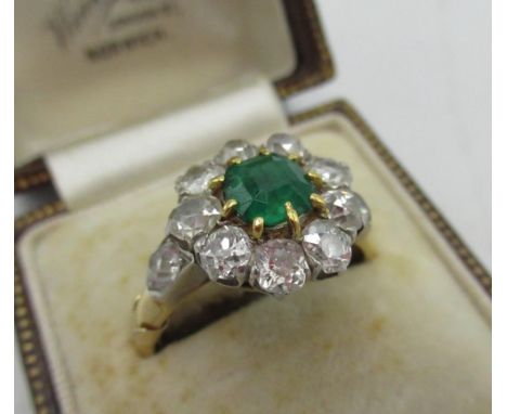 Diamond and emerald cluster ring with central cushion cut emerald, a halo of ten round cut diamonds flanked by two diamonds i