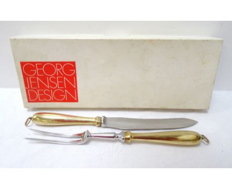 GEORG JENSEN DESIGN CARVING SETcomprising a carving knife and fork with brass handles and hanging eyes, with a wooden wall mo