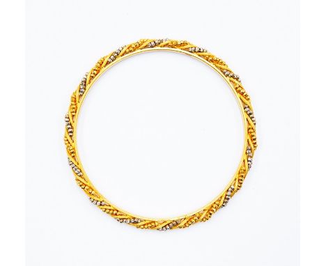 A yellow and white metal continental bangle, alternate swirling rows of yellow and white bead decoration, testing as&nbsp; 22