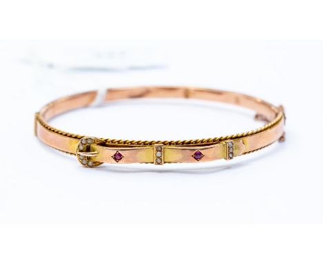 A 9ct rose gold late Victorian early Edwardian bangle set with rubies and seed pearls in the form of a buckle and bow design,