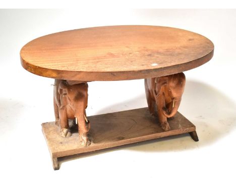 A carved wooden oval top side table, the supports in the form of elephants with bone inlaid eyes and trunks, on a plinth base