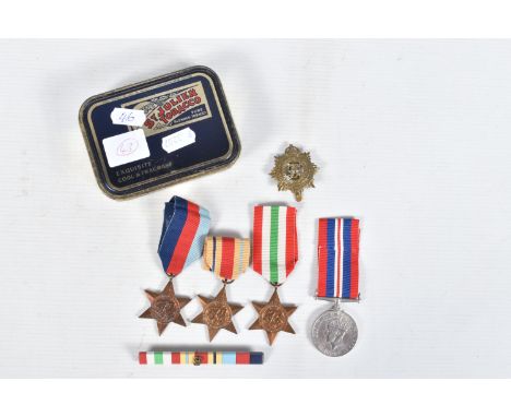 A TIN CONTAINING FOUR WWII MEDALS, a ribbon bar and a cap badge, the medals are all un-named and consist of 1939-45 star, 19-