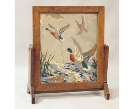 An early 20thC oak framed firescreen, the centre embroidered with ducks in flight flanked by plain supports on shaped feet, a
