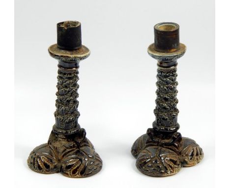 A pair of Martin Brothers candlesticks, each with a later gilt metal sconce, a leafy column and triform base, decorated with 
