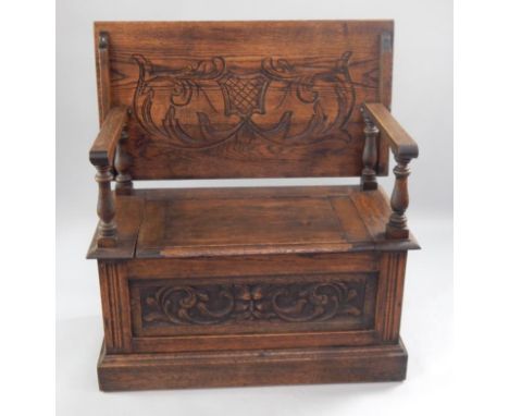 An oak monk's bench, with carved scroll decoration to the back/lid and with mask head and scroll decoration to the panelled f