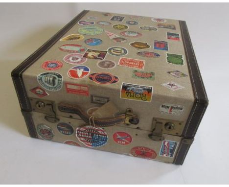 A hanging wardrobe trunk, mid 20th century, in fibre with leather mounts and fitted interior, covered in paper travel labels,