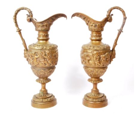 Two vintage 20th-century brass repoussé ewers, ornately decorated in cherub figures, grapes, leaves, and a devil's head to th