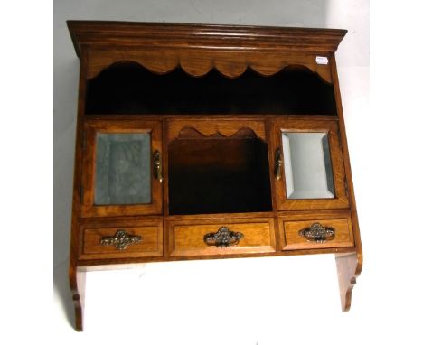 An early 20th century oak smokers cabinet with shelf over two lower mirror doors, a central aperture over three small drawers