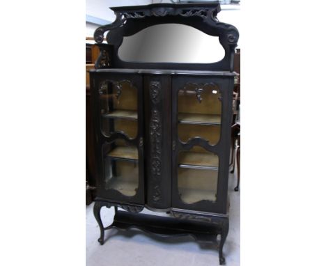 A late 19th early 20th century ebonised twin door display cabinet, central carved panel flanked by two glazed doors enclosing