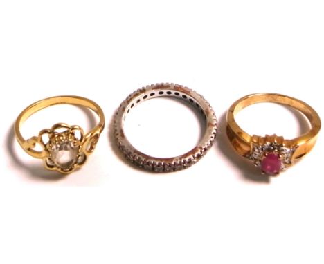 A white metal ring set with white stones, a yellow metal ring set with central red stone and a yellow metal scrolling ring se