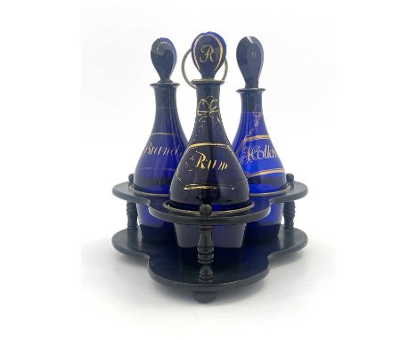 Three Bristol blue and gilt glass spirit decanters in ebonised wooden stand, circa 1790, Indian Club form, each with a painte