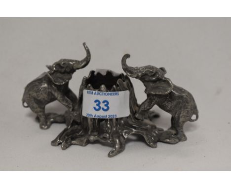 A white metal candlestick having elephants flanking a tree stump.