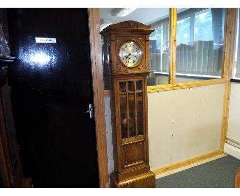 An early 20th century grandmother clock, the light oak case having glazed opening door displaying the brass pendulum, carved 