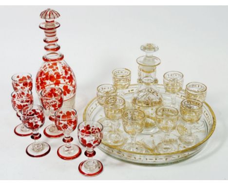 Two coloured glass liqueur sets consisting of one gilt ribbon design example with circular tray, decanter and nine glasses, t