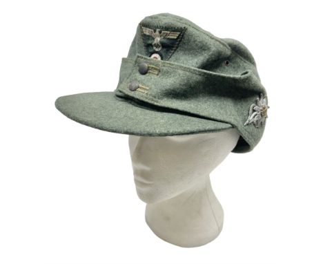 WW2 German Army M43 field cap with triangular cloth eagle and roundel badge and metal edelweiss badge for mountain troops; fa