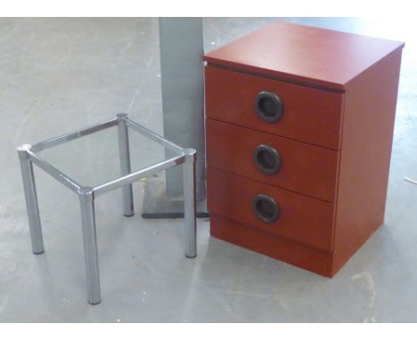 A GLASS TOPPED SQUARE COFFEE TABLE ON METAL TUBULAR LEGS AND A WOOD EFFECT SMALL CHEST OF THREE DRAWERS WIT ROUND HANDLES, 1'