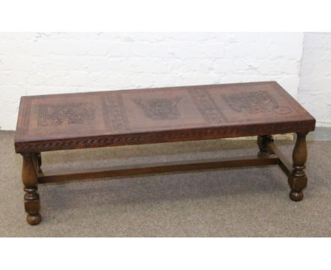 An oak coffee table raised on turned baluster supports and with tooled leather top decorated with Inca style figures.