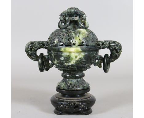 A Chinese carved jade twin handled censor and cover raised on a hardwood plinth with seperatly carved ring mouldings and styl