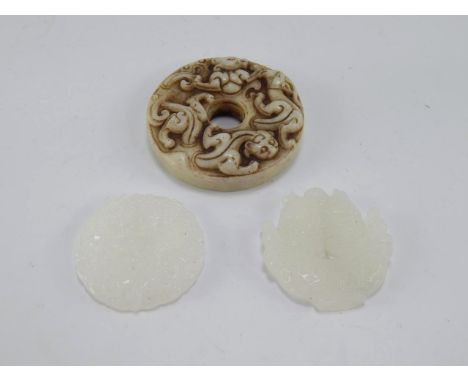 A Chinese jade pi disc carved with salamanders, 6cm diameter, and two white jadite carvings of fish in a bowl, and a dragon, 