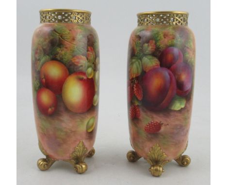A pair of Royal Worcester cylindrical shaped vases, painted half round with fruit by Townsend, with pierced necks, raised on 