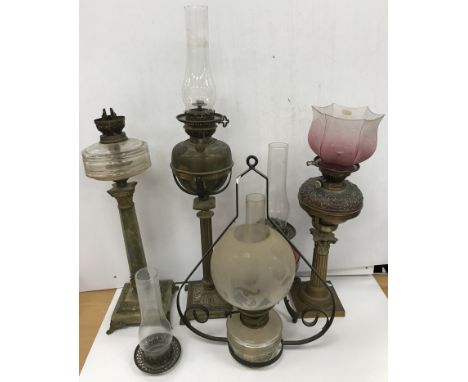 A collection of five various oil lamps including a Corinthian column lamp with embossed copper reservoir and graduated cranbe