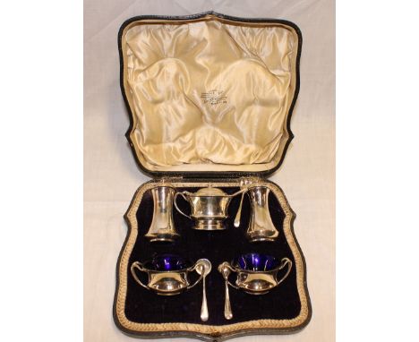 A George V silver five piece cruet set comprising a pair of circular two handled salts with blue glass liners, pair of matchi