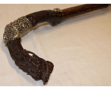 An unusual Burmese carved teak walking cane, the handle ornately carved in the form of a dragon's head with silvered collar m