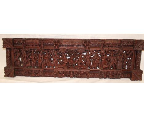 A Burmese carved teak rectangular panel decorated in relief with numerous figures, 30½" long