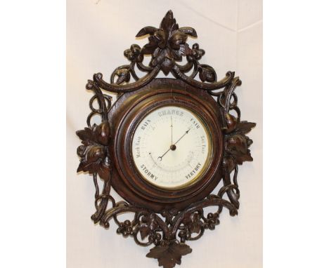 A Black Forest aneroid barometer with ceramics circular dial in carved wood fruit and leaf decorated case, 21" high 