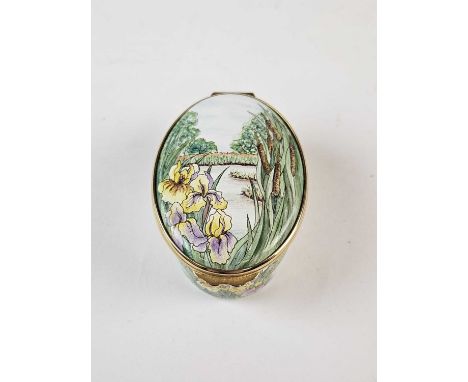 A Moorcroft enamel oval trinket box, circa 2000, painted with flowers and bulrushes, with a lake beyond, 6.5cm long x 4.5cm w