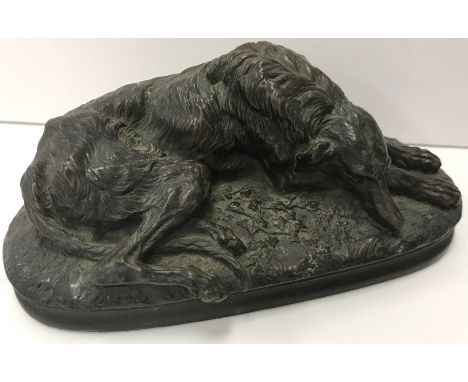 A bronze study of a recumbent Lurcher type dog on an ivy covered base, signed "M. Dava", 15 cm wide x 6 cm high