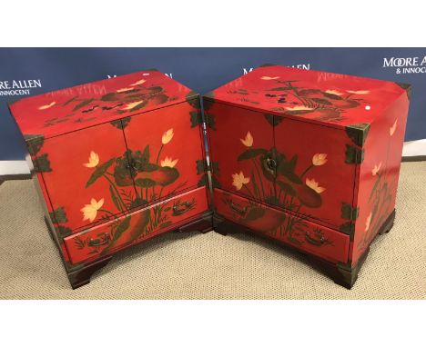 A pair of modern Chinese red lacquered dwarf cupboards, decorated with lilies and ducks, the two cupboard doors opening to re