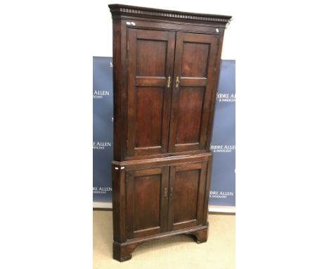 A 19th Century oak free standing corner cupboard, the dentil cornice over two twin panelled doors enclosing two shelves on a 