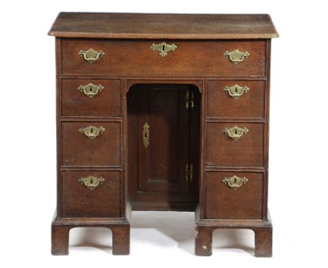 A GEORGE II OAK KNEEHOLE DESK C.1730-40 with a caddy moulded edge top above an arrangement of seven drawers around a cupboard