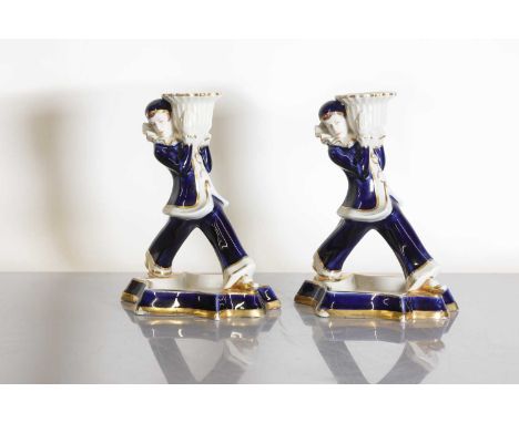A pair of Royal Dux Art Deco candlesticks,each modelled as a harlequin holding sconces, raised on dished star plinths, stampe