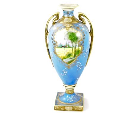 A Noritake porcelain two handled pedestal vase, handpainted with reserves of landscape decoration on a lavender blue ground, 