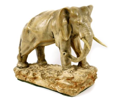 An early 20thC pottery figure of an elephant, on a rock work base, with trunk lowered, baize lined, numbered to the back, 40c