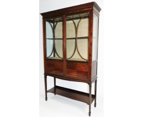 An Edwardian mahogany display cabinet, the fixed dentil cornice raised above a pair of astragal glazed doors with panels bene