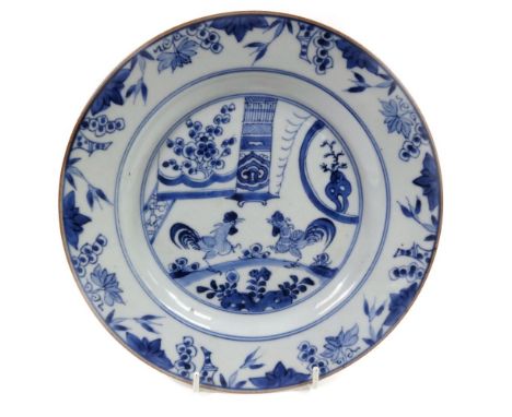 An 18thC blue and white Delftware plate, decorated with a cock fighting scene before flowers, with an outer floral and yellow