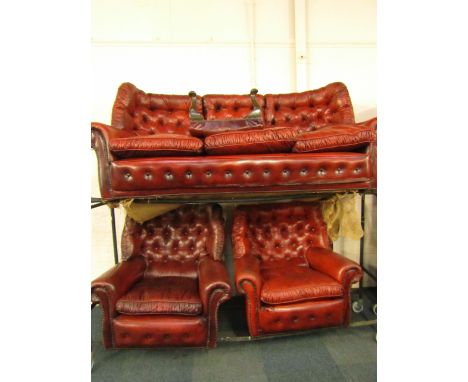 A red leather button back and brass studded three piece suite, comprising three seater sofa and pair of armchairs on castors,