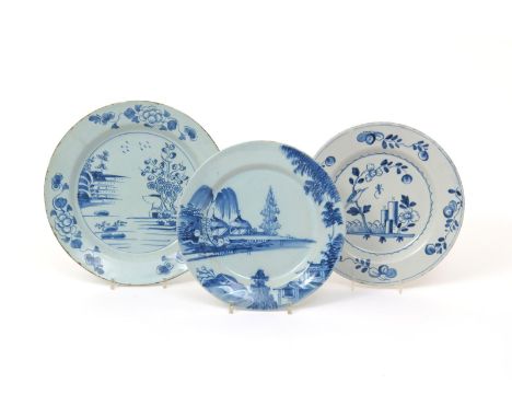 Three English delftware plates, 18th century, one painted with low huts beneath willow at the water's edge, one with a bird p